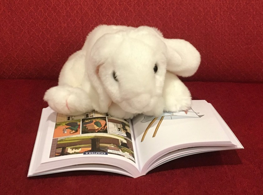 Marshmallow is reading Kristy's Great Idea (The Baby-Sitters Club Graphic Novels #1) by Ann M. Martin and Raina Telgemeier.