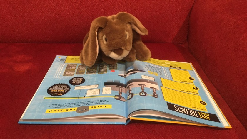 Caramel is reading "Caught in the tractor!" in How Things Work by T. J. Resler.