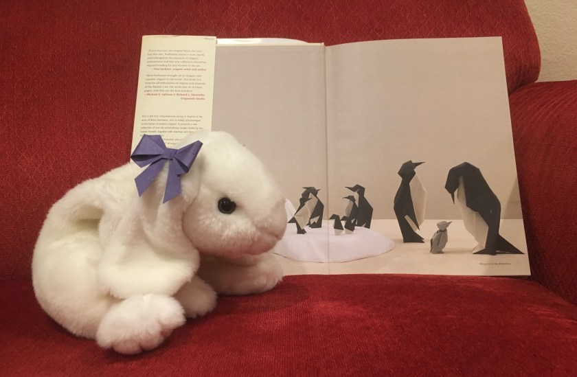 Marshmallow is pointing to the inside cover pages of Akira Yoshizawa: Japan’s Greatest Origami Master, with text, diagrams, and models by Akira Yoshizawa.
