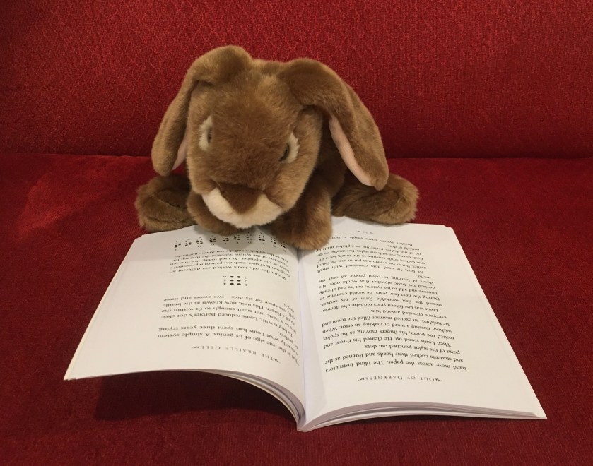 Caramel is reading Out of Darkness: The Story of Louis Braille, written by Russell Freedman and illustrated by Kate Kiesler He is on the page where the Braille alphabet is being described. .