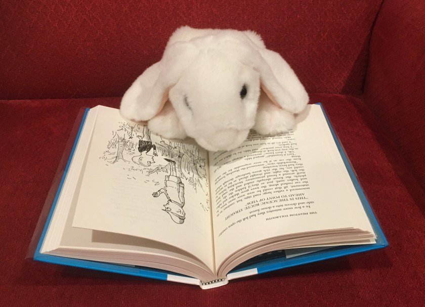 Marshmallow is reading The Phantom Tollbooth, written by Norton Juster and illustrated by Jules Feiffer.