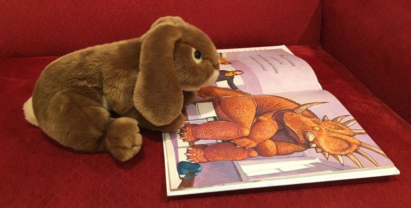 Caramel is reading How Do Dinosaurs Get Well Soon? (2003),  written by Jane Yolen and illustrated by Mark Teague. 