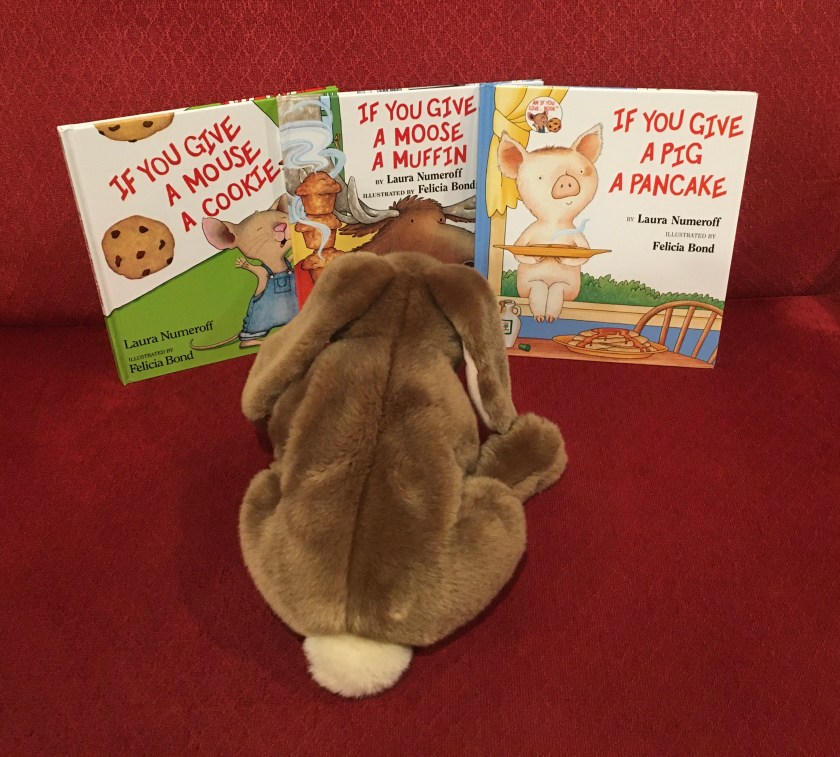 Caramel is looking at If You Give a Mouse a Cookie (1985), If You Give a Moose a Muffin (1991), and If You Give a Pig a Pancake (1998), all written by Laura Numeroff and illustrated by Felicia Bond.