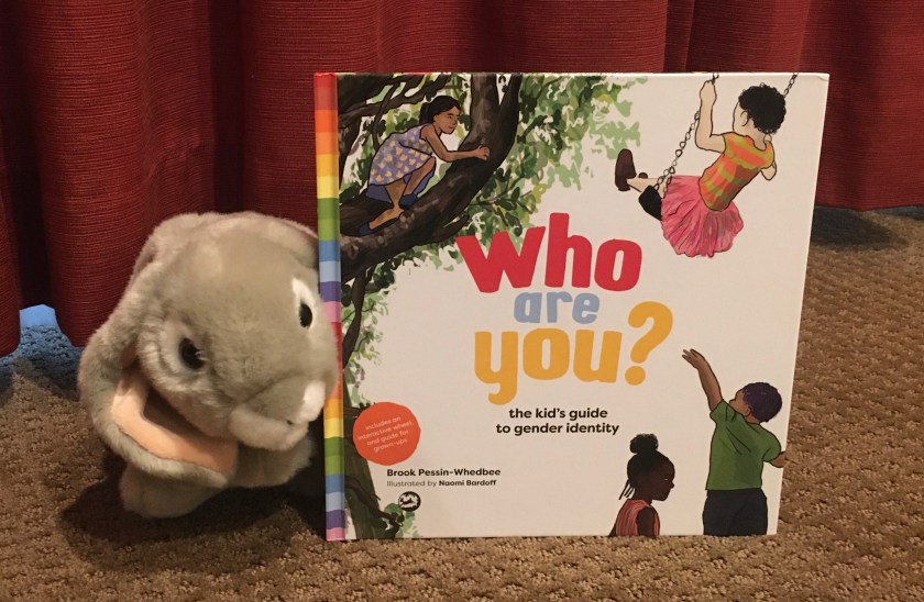 Sprinkles poses with a copy of Who Are You? The Kid's Guide to Gender Identity, written by Brook Pessin-Whedbee and illustrated by Naomi Bardoff.