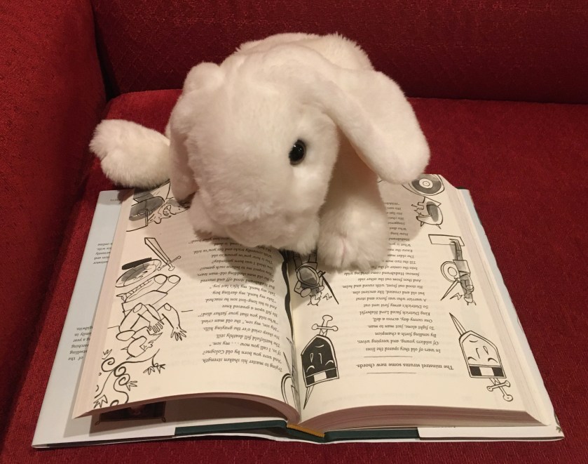 Marshmallow is reading The Song of Hildebrand in The Inquisitor's Tale: Or, The Three Magical Children and Their Holy Dog, written by Adam Gidwitz and illuminated by Hatem Aly. 