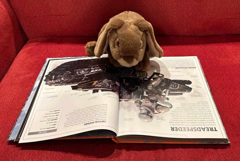 Caramel is reading Star Wars: Complete Vehicles - New Edition, written by Kerrie Dougherty, Jason Fry, Pablo Hidalgo, David West Reynolds, Curtis Saxton, and Ryder Windham, and illustrated by Richard Chasemore, Hans Jenssen, John Mullaney, Kemp Remillard, and Jon Hall. He is looking at the page on the treadspeeder, his favorite Star Wars vehicle.