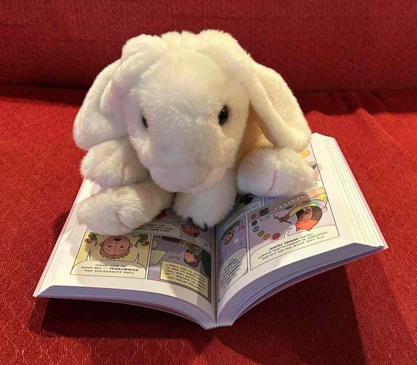 Marshmallow is reading The Cartoonists Club by Raina Telgemeier and Scott McCloud.