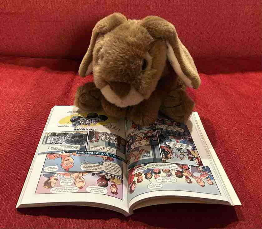 Caramel is reading Spaced Out: The Graphic Novel by Stuart Gibbs and Ward Jenkins.